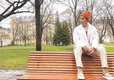 a young man sitting on top of a wooden bench in a park next to trees