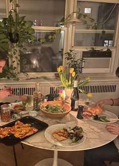 two people sitting at a table with plates of food in front of them and plants on the window sill