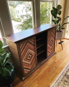 a wooden cabinet sitting on top of a hard wood floor next to a potted plant