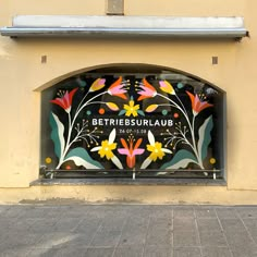 an artistic window with flowers painted on the glass and below it is a sign that reads betrie dessaulaue