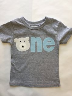 a t - shirt that says one with a teddy bear on the front and blue letters across the chest