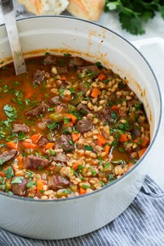 a pot filled with meat and vegetable soup on top of a table next to bread