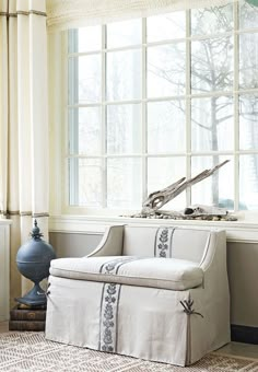 a white couch sitting in front of a window next to a blue vase and lamp