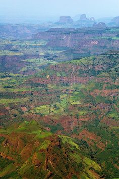 an aerial view of mountains and valleys in the distance with green grass on each side