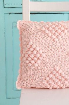 a pink crocheted pillow sitting on top of a white chair next to a blue door