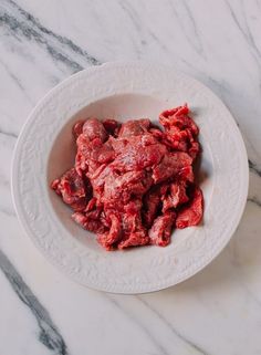 a white plate topped with meat on top of a marble counter