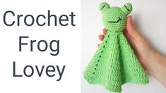 a hand holding a green crochet frog toy with the words crochet frog lovey on it