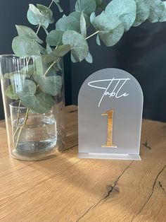 a table with a glass vase filled with water and a sign that says it's 1