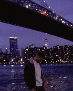 a man standing in front of the water with a city skyline behind him at night