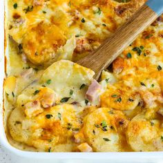 a casserole dish with potatoes, ham and cheese in it next to a wooden spoon