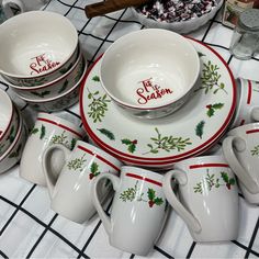 a table topped with white dishes and cups filled with christmas decorations on top of a checkered table cloth