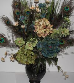 a black vase filled with lots of flowers and peacock feathers on top of a table