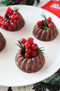 four small chocolate cakes on a white plate with cherries and rosemary sprigs