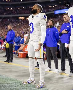 a football player is standing on the sidelines with his hands in his pockets and looking off into the distance