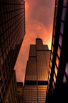 looking up at skyscrapers from the ground with clouds in the sky behind them and an orange sunset