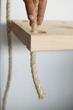 a person is pulling rope from a wooden shelf to the floor with their hands and fingers