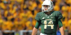 a football player in green and white uniform standing on the field with his mouth open