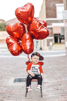 a little boy sitting on top of a chair holding red balloons