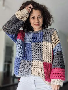 a woman wearing a multicolored sweater and white jeans stands with her hands on her head