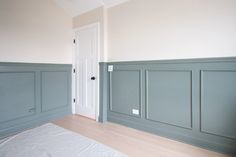 an empty room with wood flooring and green painted paneling on the walls, along with a white door