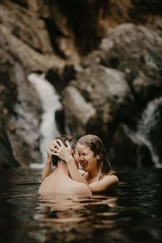 a man and woman are in the water near a waterfall, one is holding his head