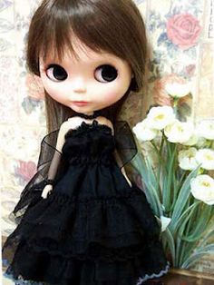 a doll is standing next to a vase with flowers in it and wearing a black dress