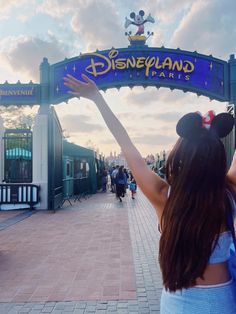 a woman holding her arms up in front of the entrance to disney land