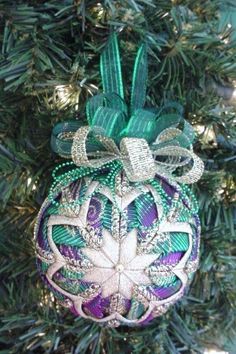 an ornament hanging from a christmas tree decorated with green and purple beads, ribbons and bows