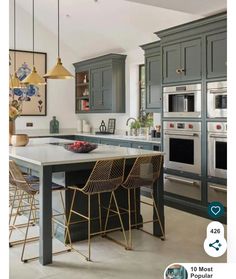 an image of a kitchen setting with grey cabinets and gold bar stools in the center