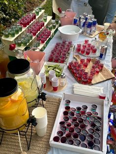 a table topped with lots of cups filled with liquid next to bottles and containers full of fruit