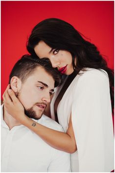 a man and woman embracing each other in front of a red background