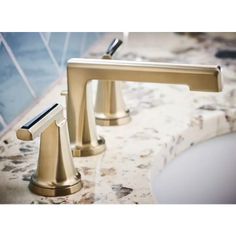 two gold faucets on a marble counter top