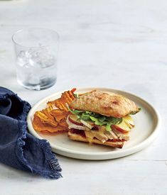 a sandwich and potato chips on a white plate next to a glass of water with a blue napkin