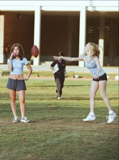 two girls are playing with a football in front of a building and one girl is throwing the ball