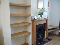 there is a fireplace in the corner of this living room with shelves on either side