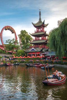 two people are sitting in a small boat on the water near an amusement park ride