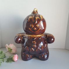 a brown bear statue next to a pink rose on a white surface with a wall in the background