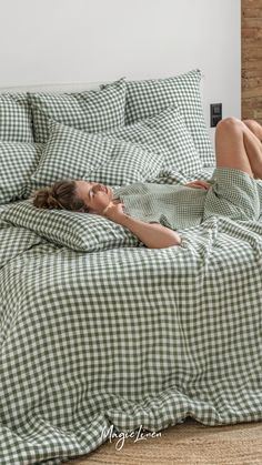 a woman laying on top of a bed covered in green checkered sheets and pillows