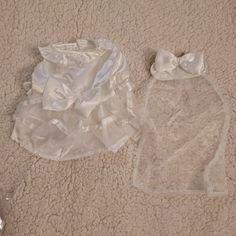 two baby clothes laying on the floor next to each other, one with a bow