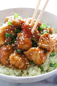 a white bowl filled with rice and meat covered in sesame seeds topped with chopsticks