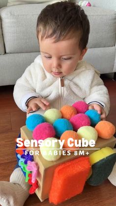 a small child sitting on the floor playing with colorful balls in a cardboard box that is filled with stuffed animals