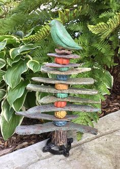 a bird sits on top of a tree made out of rocks and stones in front of some plants