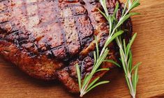 a piece of meat on a cutting board with some rosemary sprigs next to it