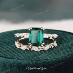 an emerald and diamond ring sitting on top of a green velvet cushioned hat box