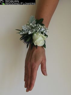 a person's hand holding a bouquet of white and blue flowers on their wrist