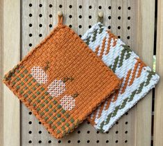 two orange and white knitted items hanging from pegs on a wooden board with holes in it