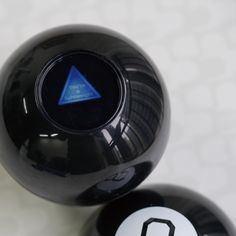 two black balls sitting next to each other on a white surface with one blue triangle in the middle