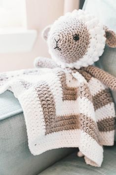 a crocheted sheep is sitting on a couch with a blanket draped over it