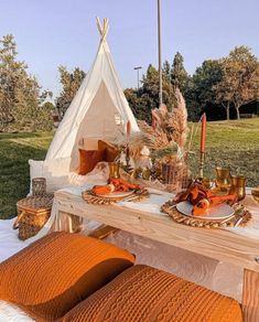 an outdoor table set up with orange pillows and place settings for two people to eat