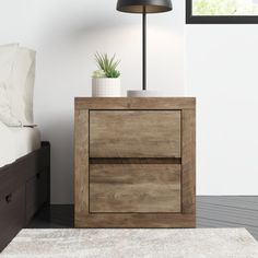 a nightstand with a plant on top of it next to a white rug and bed